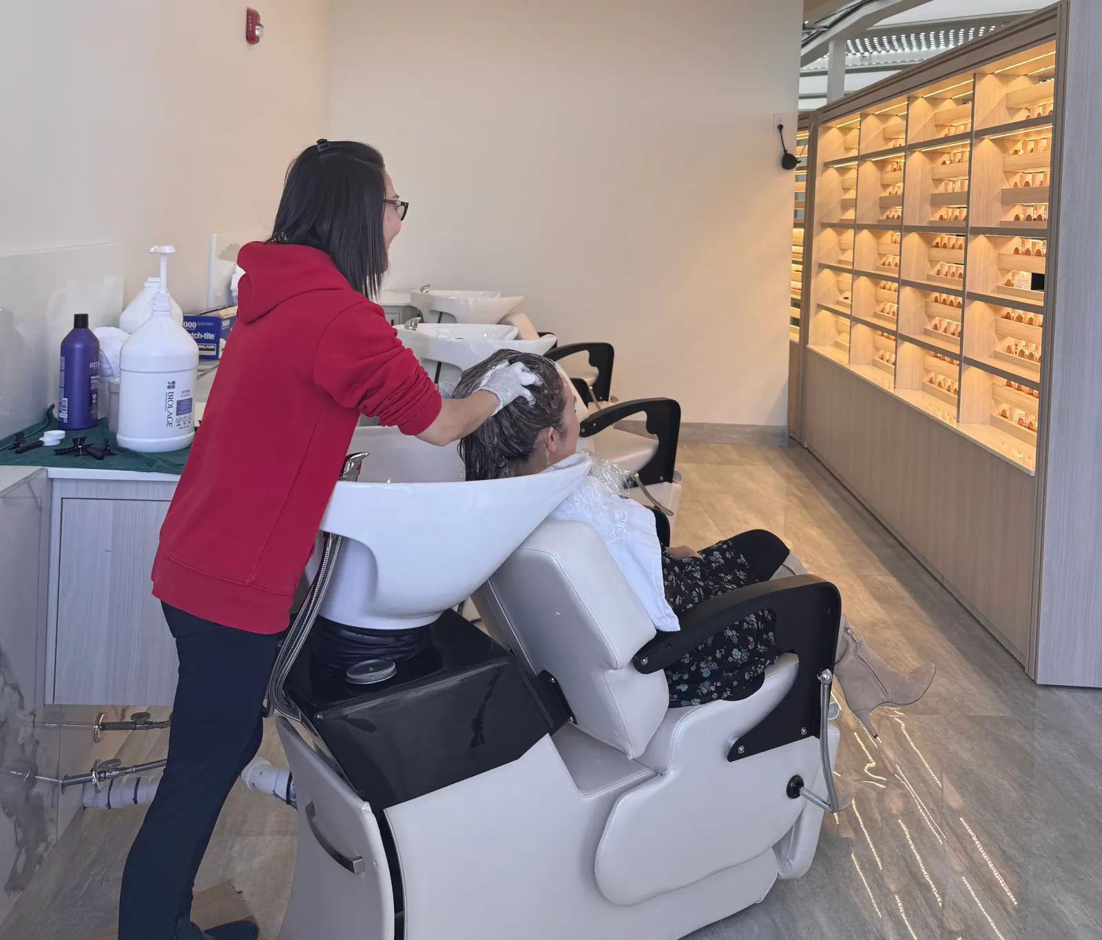 A stylist with gloved hands working on a client’s hair at the shampoo bowl