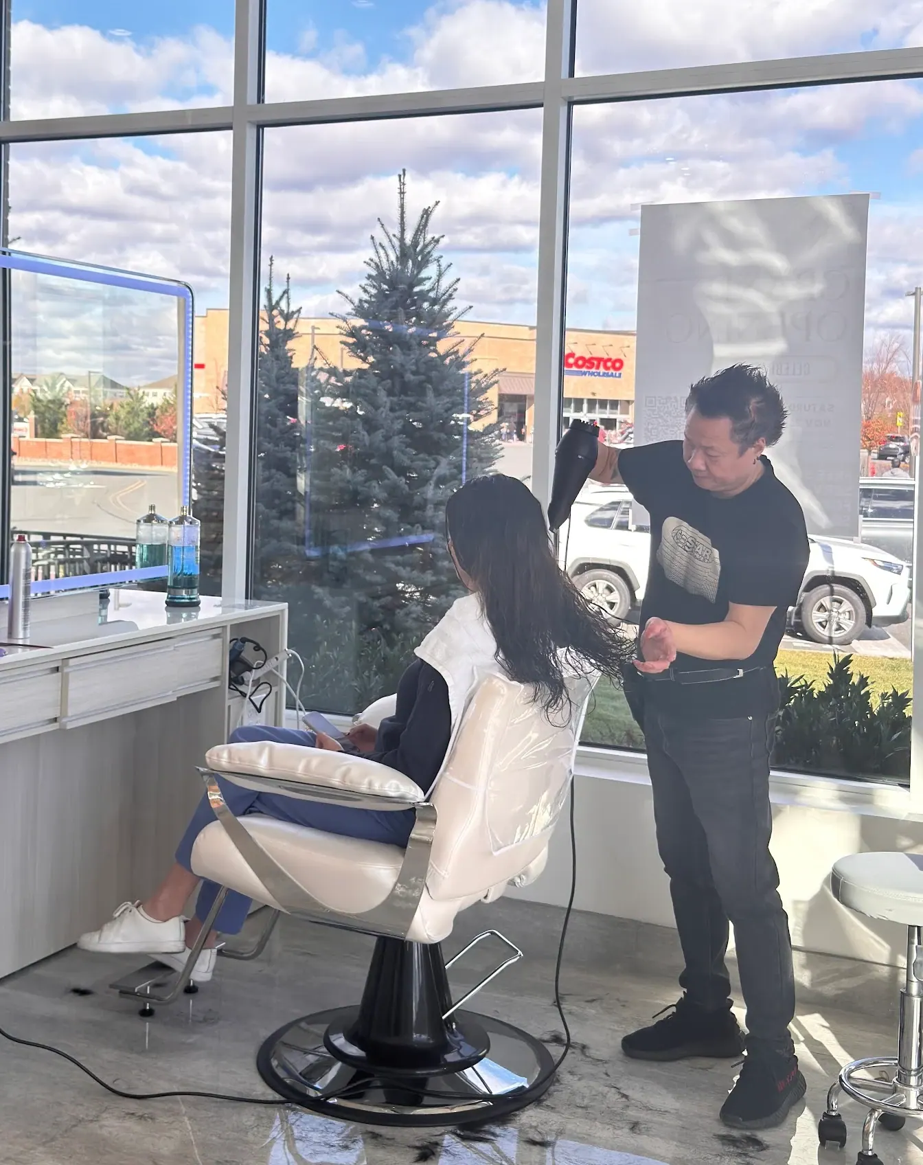 A stylist blow-drying a client’s long hair by the front windows at Innovate Salon & Spa
