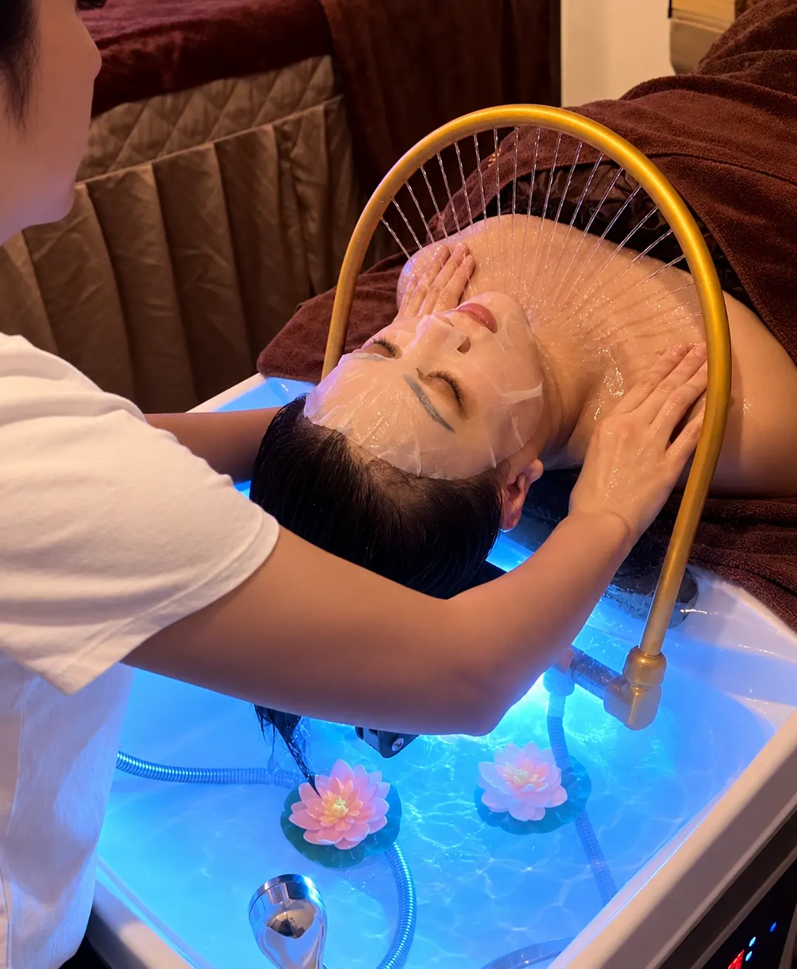 A therapist massaging a guest's scalp under the head spa water arc